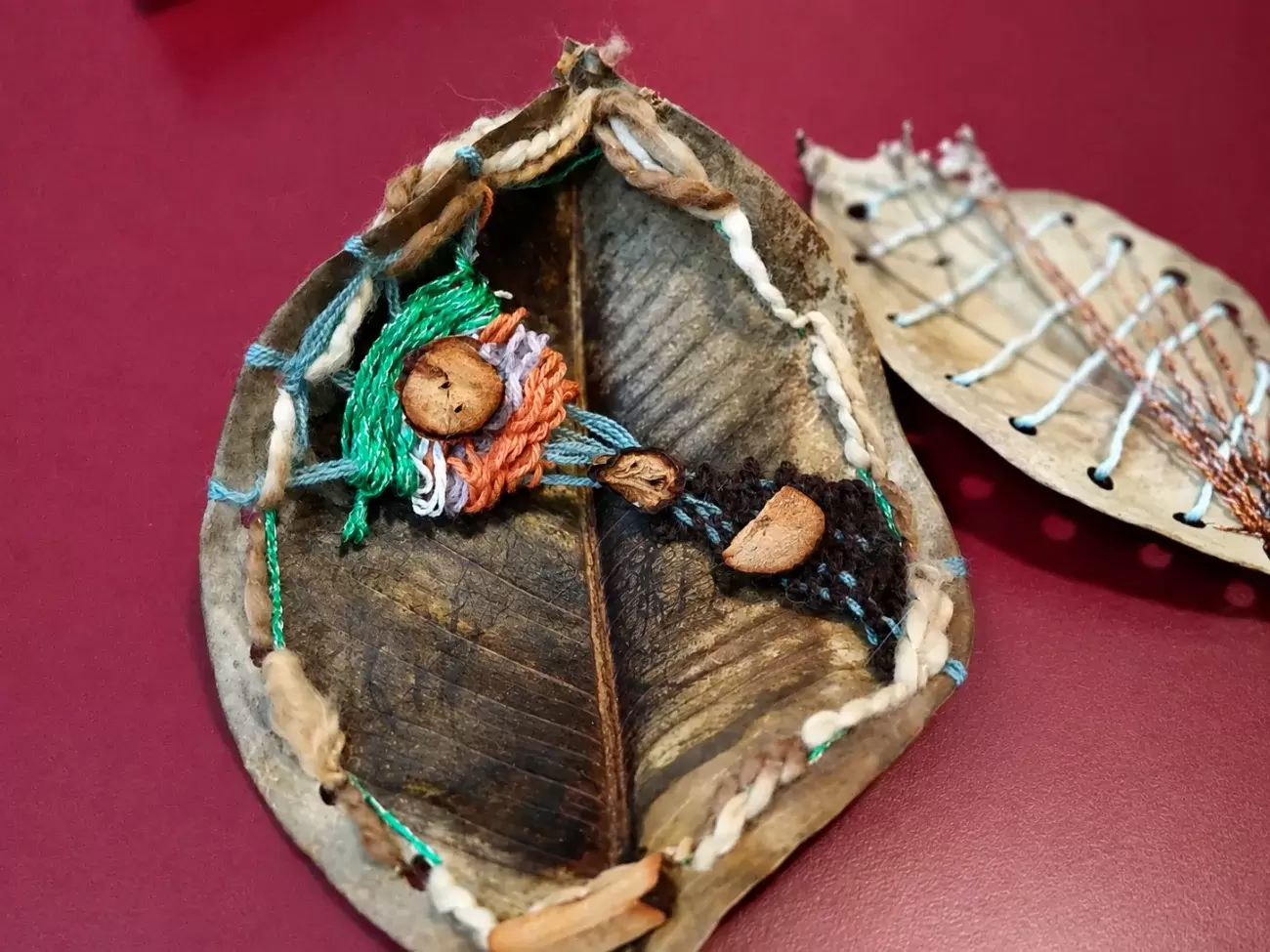 Detalle de una hoja tejida con hilos de colores, botones de madera y texturas naturales