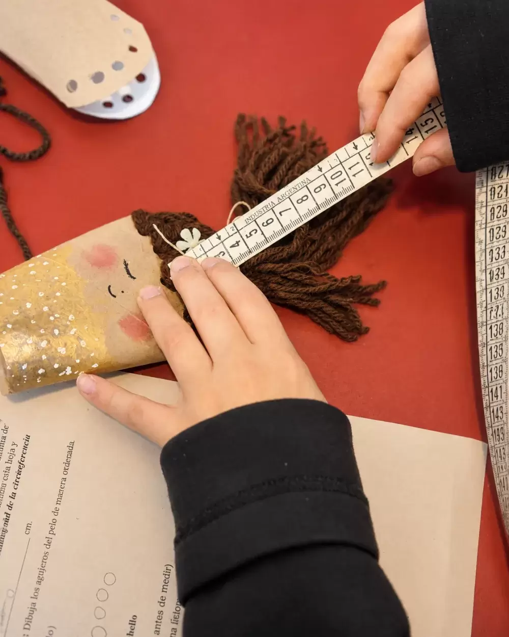 Tomando medidas con cinta métrica para armar el cabello de una muñeca de cartón