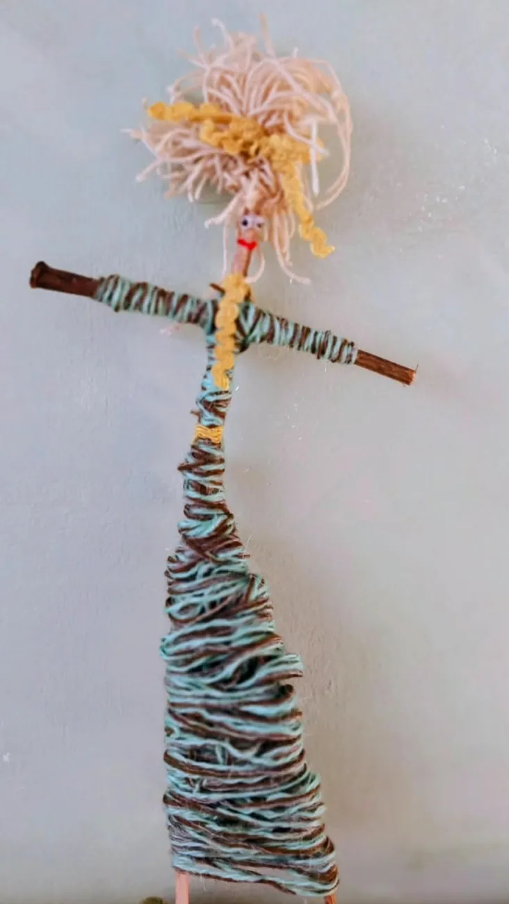 Muñeca de lana tejida sobre ramas, con cabello de hilo y vestido en punto envolvente